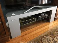 TV stand with silver metal frame and glass shelf, Toshiba DVD player, HBO DVD set on shelf beneath TV