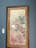 Full view of one framed floral artwork with pink, blue and white flowers on beige background in gold frame with corner accents