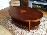 Angle view of coffee table showing curved top with inlaid wood pattern and lower tier with storage drawers and metallic handles.