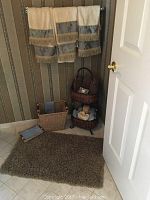 Hand towels, bath mat on floor, two-tier wicker basket, woven trash bin, and napkin holder in bathroom corner.