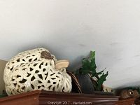 Carved ceramic jug with cut-out design and some faux ivy plant leaves visible, placed on wooden furniture top