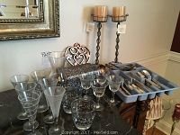View of mixed glassware including various glasses and goblets, decorative metal box, two pedestal candle holders, and flatware in organizer tray