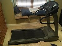 Full side view of treadmill in a room with a window bench and chest of drawers, showing running belt and base unit.