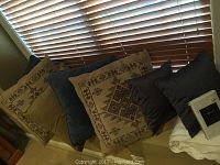 Photo showing three beige embroidered large accent pillows, two solid navy blue large accent pillows, two smaller black throw pillows, white king size quilt partially visible, and new white pillowcase set in packaging.