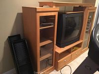 Entertainment center front view with TV in center, glass cabinets on sides, and drawers below.