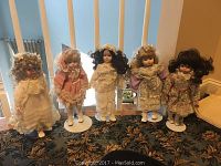 Five dolls standing in a row on a floral carpet with window background.