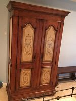 Front view of the wooden armoire showing the antiqued finish and painted inlay panels on the doors.