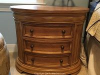 Front view of one solid wood oval nightstand with three drawers and round knobs