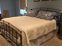 Full view of king size metal bed frame with mattress and linens on it, showing headboard and footboard.