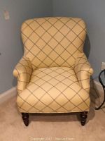 Front view of beige upholstered armchair with blue criss-cross pattern and wooden legs.