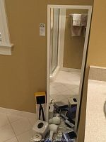 Full-length mirror leaning against wall with various hair care tools and bathroom accessories placed on floor in front and around it.