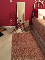 Red painted metal folding chair with cushion next to full-length white framed mirror, wicker waste basket and 3x5 woven area rug on carpet floor