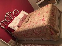 Full bed with ornate white metal headboard and floral mattress cover, pillows styling shown for display