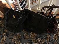Three leather handbags side by side on a carpet. Two black and one brown.