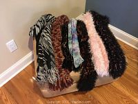 Overall view of six women's scarves displayed draped over a small piece of furniture showing a variety of colors and textures.