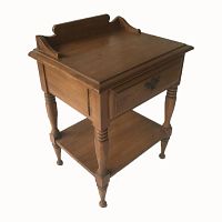 Side angle of antique wooden wash stand showing the raised backsplash, turned legs, drawer with metal handle, and lower shelf.