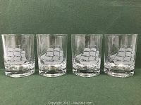 Four clear double old fashioned glasses in a row on green background showing sailing ship etching on each