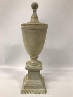 Front view of the painted metal urn showing its rounded finial lid, tapered body, pedestal and tiered base with relief detailing, against a white background.