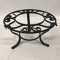 Side angle view of the round cast iron plant stand showing scrollwork detail and three curved legs.