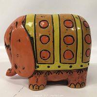 Side view of the orange ceramic elephant bank with yellow and red painted details.