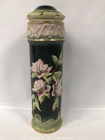 Photo of ceramic lamp base with pink flower designs on dark background and ornamental green and gold top and bottom edges.
