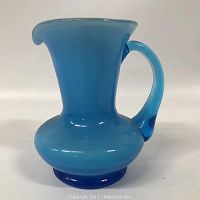 Front view of the opaque blue art glass pitcher showing the rounded body and curved handle.