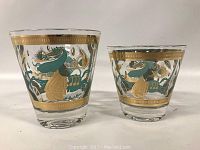 Two clear glass cocktail glasses with gilt and green decorative motifs on sides arranged side-by-side
