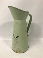 Side angled view of the seafoam painted metal pitcher showing the handle, spout, and some rust near the bottom.