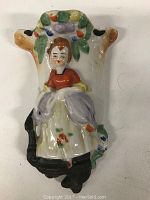 Front view of ceramic wall pocket with figurine of woman in bonnet and apron with floral decorations.