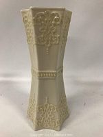 Front view of cream-colored hexagonal Belleek vase with raised floral design and beaded detailing
