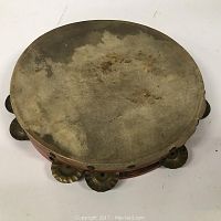 Top view of the antique tambourine showing worn and stained drum skin and partially visible metal jingles around the edge.