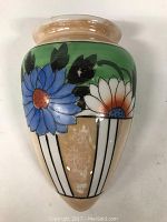 Front view of ceramic wall pocket planter showing colorful floral design with large blue and white flowers and green background.