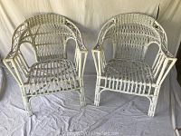 Front view of the pair of white wicker arm chairs showing woven design and structure.