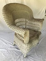 Front angle view of an antique white wicker armchair showing detailed wicker weaving and structural design with noticeable wear on the armrests.