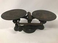 Front-facing view of the antique cast iron balance scale with visible round plates and balance beam with sliding weight.