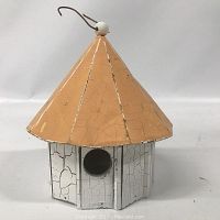 Front view of wooden birdhouse showing orange roof and white painted body with single round entrance hole.