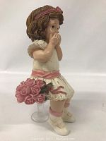 Side view of the painted cast figurine showing sitting girl with brown hair, white dress with pink details, holding pink roses and supported by a clear plastic stand.