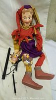 Marionette Jester Pro seated showing full body with colorful costume and attached control rods.