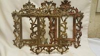 Six old ornate cast metal picture frames arranged in layered rows, antique finish, visible rust and patina.