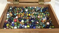 Top view of the open wooden box filled with numerous colorful vintage glass marbles of varied sizes and patterns.