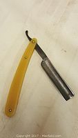 Antique German straight blade razor opened showing the steel blade and yellow handle