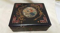 Top view of the square Asian lacquer cigarette box showing painted circular motif and ornamental decorations with visible surface wear.