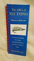 Blue cover of The ABCs of Fly Tying book by Maurice Beliveau, showing title and fishfly illustration.