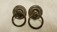 Two vintage metal ring pulls shown against white fabric background with visible patina and wear.