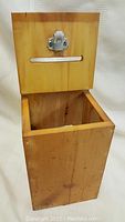 Front view of open wooden ballot box showing slot and latch on lid