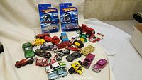 Group photo of the die cast toy cars, motorcycles, trucks and two Hot Wheels cars in packaging on a white surface.