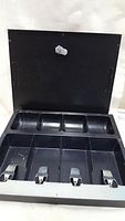 Open cashbox showing multiple compartments for organizing cash with four metal clips for bills and a smaller section for coins.