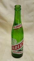Green vintage soda bottle with Elders branding on front, standing upright on neutral background.