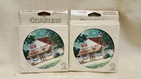 Two packs of NatureStone Coca-Cola coasters sealed in original packaging with illustrated storefront design.