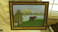 Photo of the 28x22 inch framed folk art painting by Doc Slack, showing a moose, tree, water, mountains, and sun painted on outside of the glass.